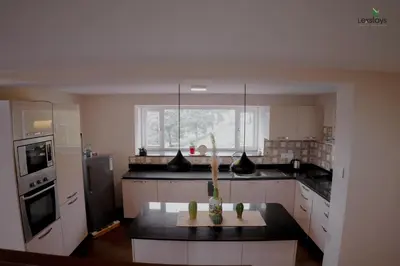 a kitchen with white cabinets and a black counter top at Yellow Tulip Hill Side Luxury Villa by LexStays in Coonoor