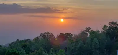 a sunset over a forest of trees with the sun setting at KSTDC Hotel Mayura Biligiri, BR Hills in Honganūr