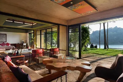 a living room with tables and chairs and a large window at StayVista at Toya Toya River View in Kozhikode