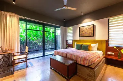 a bedroom with a bed and a desk and windows at StayVista at Toya Toya River View in Kozhikode