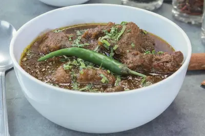 a bowl of soup with meat and a green pepper at Leela Farm Stay - Exclusive for Group Stay in Madikeri