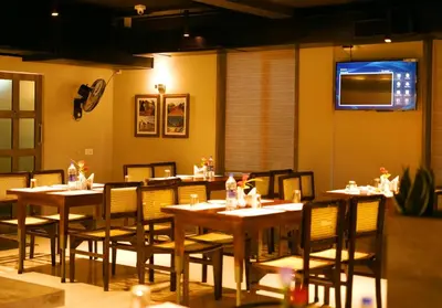 a dining room with tables and chairs and a television at WithInn Hotel - Kannur Airport in Kannur