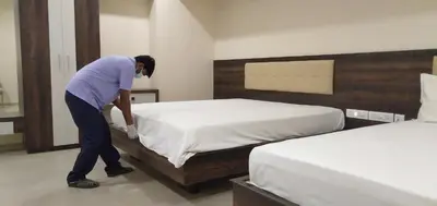 a man is making a bed in a bedroom at Ponnis Hotel in Palani