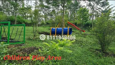 a playground with a blue barrel in the grass at Shining Caves Resort in Varagampadi