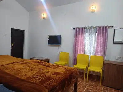 a bedroom with yellow chairs and a bed and a tv at Osprey individual Cottage in Ooty