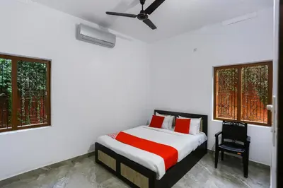 a bedroom with a bed and a chair and two windows at Hotel O Al Ameen Residency in Kannur
