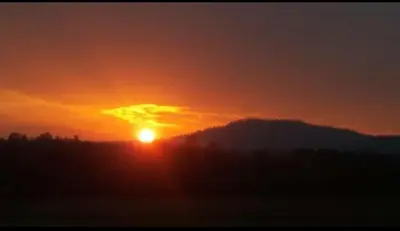 a sunset with the sun setting over a mountain at Coorg peacock feathers home stay in Kushālnagar