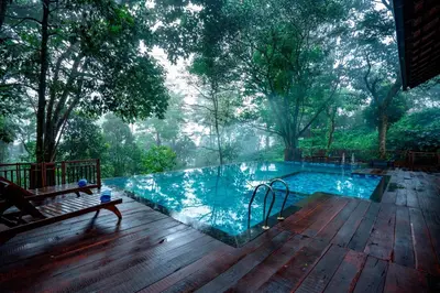 a large swimming pool on a wooden deck with trees at Vythiri Mist Resort in Vythiri
