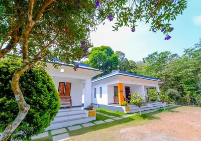 a small white house with a bench in the yard at Vythiri Silver Mist Hilltop Villa By VOYE HOMES in Vythiri