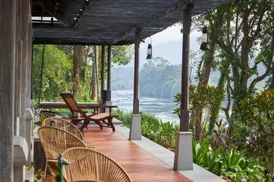 a porch with chairs and a view of the water at Periyar River Lodge in Thattakād