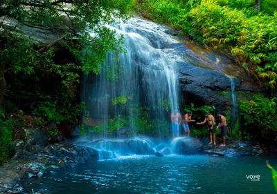 two people standing at the bottom of a waterfall at Moonlight Munnar Forest Bungalow with Private Waterfalls by VOYE HOMES in Kanthalloor