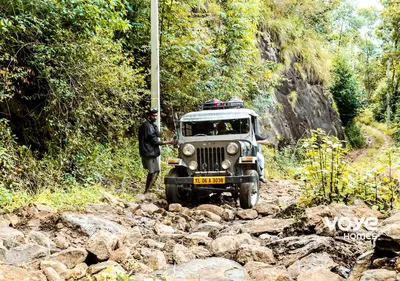 a man standing next to a jeep on a rocky road at Moonlight Munnar Forest Bungalow with Private Waterfalls by VOYE HOMES in Kanthalloor