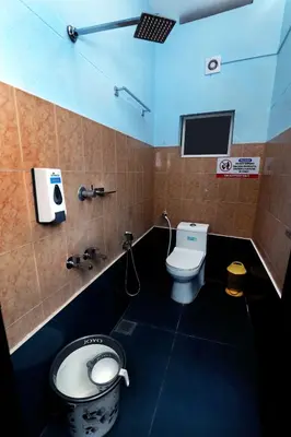 a bathroom with a toilet and a tv on the wall at NARMADA HOMESTAY Ganga in Perintalmanna