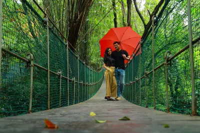 a man and woman standing on a bridge with a red umbrella at Vythiri Resort in Vythiri