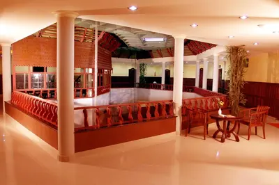 a restaurant with a bar with red chairs and a table at Devasura inn in Guruvāyūr
