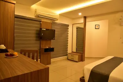 a room with a bed and a table and a television at WHITE SUITE HOTEL in Kozhikode