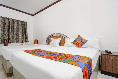 a bedroom with two white beds with a colorful blanket at Hotel Orchid Inn in Ooty