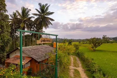 a small house on a dirt road next to a field at 5BR Firefly By The River with Breakfast - Nature's Lap in Kushālnagar