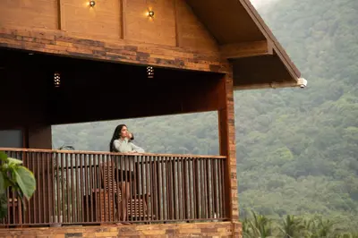 a woman standing on a balcony talking on a cell phone at Au Revoir Wellness Resort, Malampuzha in Palakkad