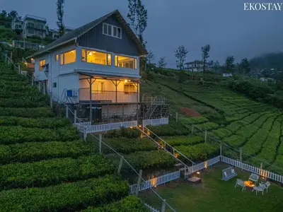 a house on a hill with lights on at EKO STAY - Woodside Ivy in Ooty