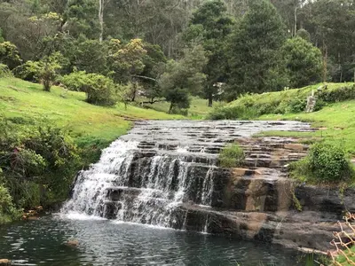 a waterfall in a field next to a pond at Kodai Countryside Homestay in Kodaikānāl