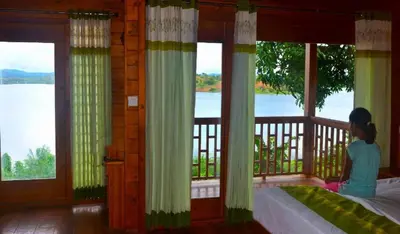 a woman sitting on a bed looking out of a window at LakeRose Wayanad Resort - Water Front Grandeur in Kalpetta