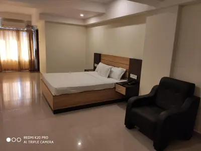 a bedroom with a bed and a black chair at Hotel Sree Gokulam Apartments in Guruvāyūr