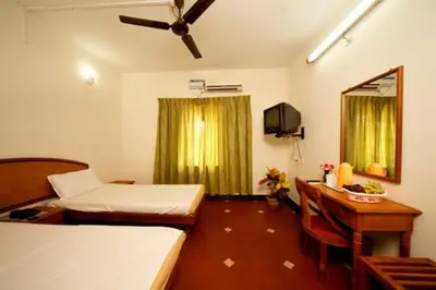 a room with two beds and a desk and a television at KTDC Tamarind, Nilambur in Nilambūr