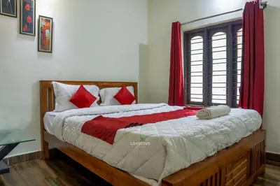 a bedroom with a large bed with red curtains at D signature Homestay By Lexstays in Kushālnagar