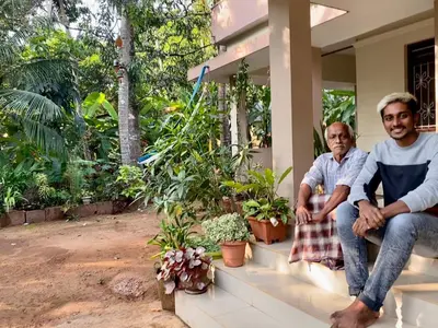 two men sitting on the porch of a house with plants at NARAYANALAYAM-Vintage Retreat-Homestay & Rest'Inn in Kannur