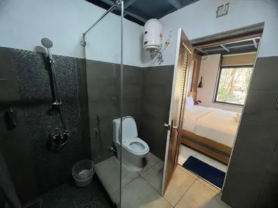a bathroom with a shower and a toilet and a bed at Wild root stay- Aster Chalet in Wayanad