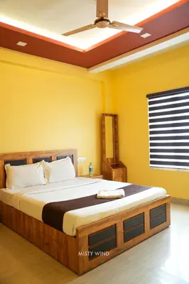 a bedroom with a large bed with yellow walls at Vythiri Misty Wind Holiday Homes in Vythiri