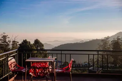 a table and chairs on a balcony with a view of mountains at Vista Suites Doddabetta Ooty By Bestinn Leisure in Ooty