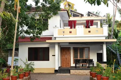a white house with red curtains in front of it at Oceangreen cottage in Kannur