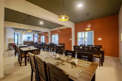 a dining room with tables and chairs and windows at Treebo Sans Sarav Kushalnagar, 10 mins to Nisargadhama Island in Madikeri