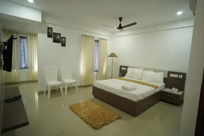 a bedroom with a bed and two white chairs at SN ROOMS in Perumbavoor