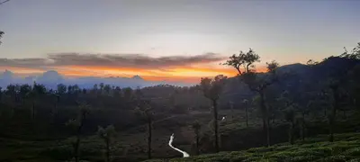 a sunset over a valley with trees and mountains at Honeybee Homestay by The Jungle Stay Groups in Vālpārai