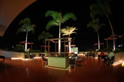 a patio with tables and chairs and palm trees at night at RATHNA RESIDENCY in Coimbatore