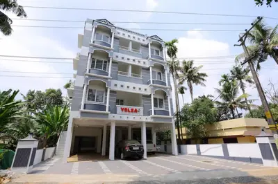 a white building with a car parked in front of it at Yelza Hotel and Residence in Alwaye