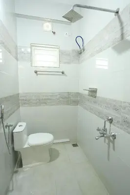 a white bathroom with a toilet and a window at Yelza Hotel and Residence in Alwaye