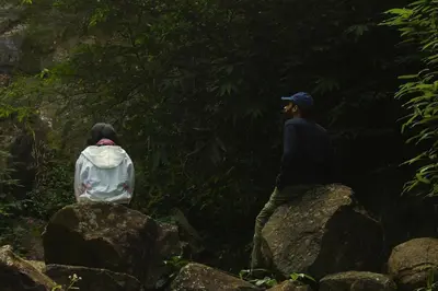 two people sitting on rocks in a forest at Skyfall 900kandi in Meppādi