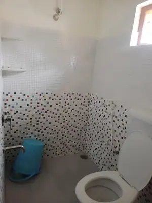 a bathroom with a toilet and a blue trash can at Krishna Kuteera in Siddapur