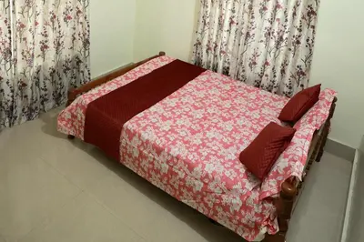 a bed in a room with a red comforter and curtains at Toms Villa along National highway Thrissur at Nadathara in Trichūr