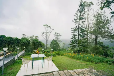 a table and chairs in a garden with a view at Wild Elephant Resort in Kallar Vattiyar