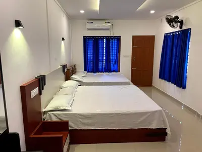 two beds in a room with blue curtains at Dakshinakasi Guest House in Thirunelli