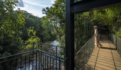 a woman standing on a bridge over a river at Klov Resort & Spa in Wayanad