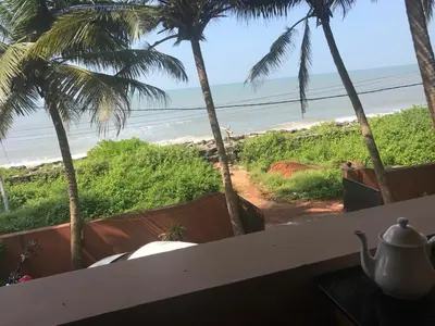 a view of the beach from a restaurant with palm trees at Kizhunna rock beach house in Kannur