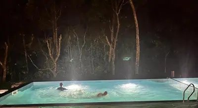 two people swimming in a swimming pool at night at Shibi's Tea Garden Heritage in Vayittiri