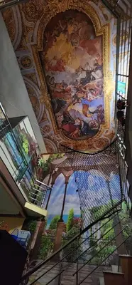 a staircase in a building with a painting on the ceiling at JJ's White House in Trichūr