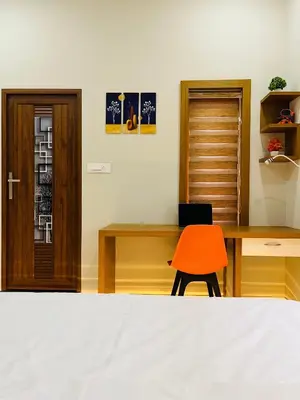 a bedroom with a bed and a desk and a orange chair at Milaano Orchids, Service Villa, Kammana Mananthavady in Wayanad